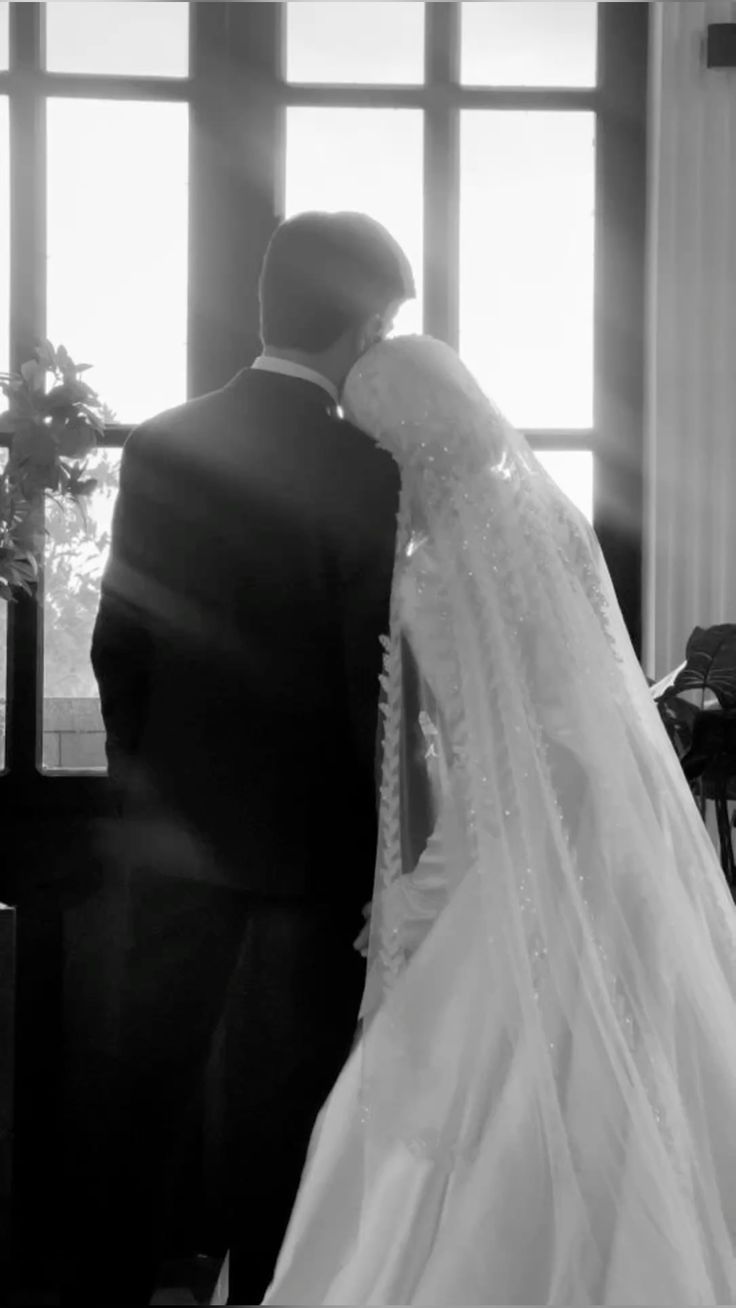 Couple de mariés à contre-jour devant une grande fenêtre, photo en noir et blanc